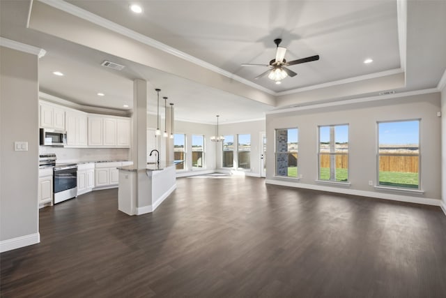 unfurnished living room featuring ceiling fan with notable chandelier, a healthy amount of sunlight, ornamental molding, and dark wood-type flooring