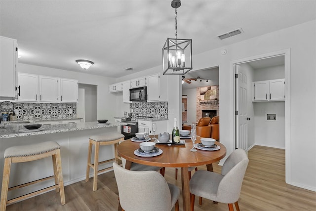 dining space featuring light wood-type flooring, an inviting chandelier, and a stone fireplace