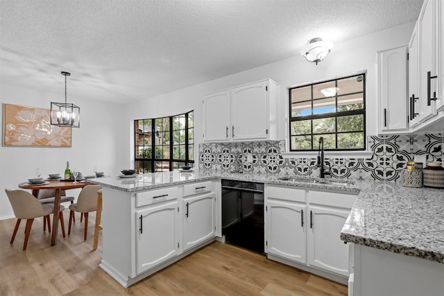 kitchen featuring kitchen peninsula, sink, decorative light fixtures, dishwasher, and white cabinetry