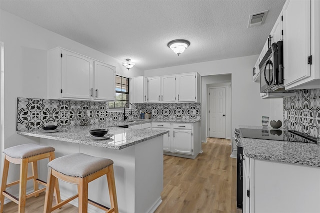 kitchen with kitchen peninsula, stainless steel electric stove, white cabinets, a kitchen bar, and light wood-type flooring