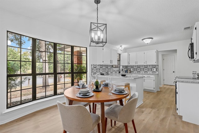 dining space with light hardwood / wood-style floors, a wealth of natural light, a notable chandelier, and sink