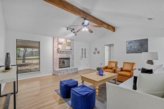 living room with light hardwood / wood-style flooring, vaulted ceiling with beams, ceiling fan, a textured ceiling, and a fireplace