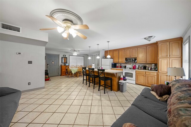 kitchen with ceiling fan, a kitchen bar, pendant lighting, a center island, and white appliances