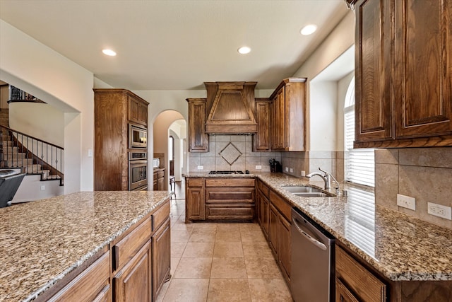 kitchen with custom range hood, sink, light stone countertops, appliances with stainless steel finishes, and tasteful backsplash