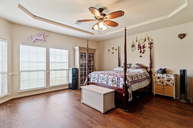 bedroom with dark hardwood / wood-style flooring, a tray ceiling, and ceiling fan