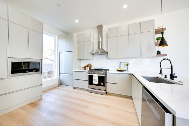 kitchen featuring sink, hanging light fixtures, wall chimney exhaust hood, light hardwood / wood-style floors, and stainless steel appliances