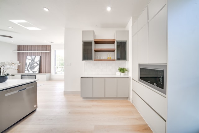 kitchen with stainless steel dishwasher, decorative backsplash, white cabinetry, and light wood-type flooring