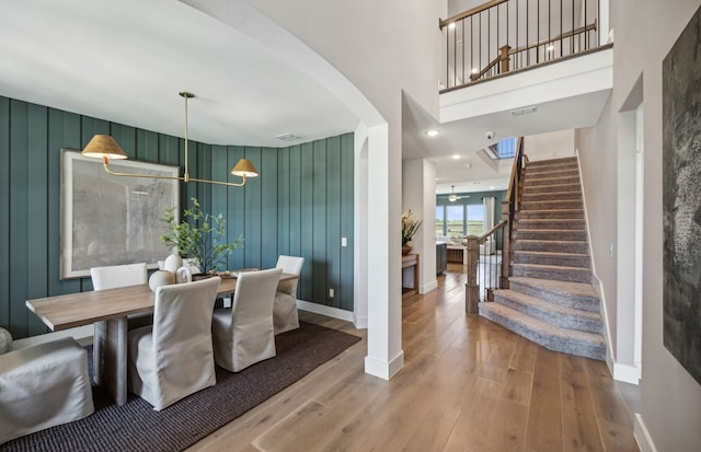 dining room featuring hardwood / wood-style floors, wooden walls, a high ceiling, and ceiling fan