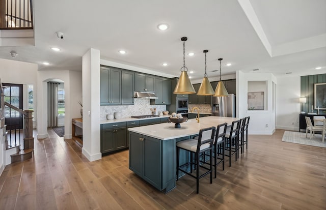 kitchen featuring a kitchen bar, an island with sink, hanging light fixtures, stainless steel appliances, and hardwood / wood-style flooring