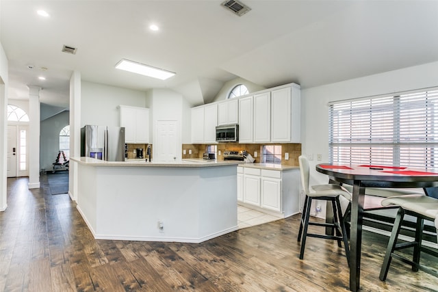 kitchen featuring hardwood / wood-style floors, white cabinetry, stainless steel appliances, vaulted ceiling, and a kitchen island with sink