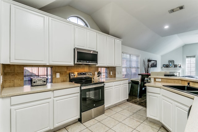 kitchen with lofted ceiling, light tile patterned floors, appliances with stainless steel finishes, white cabinetry, and sink