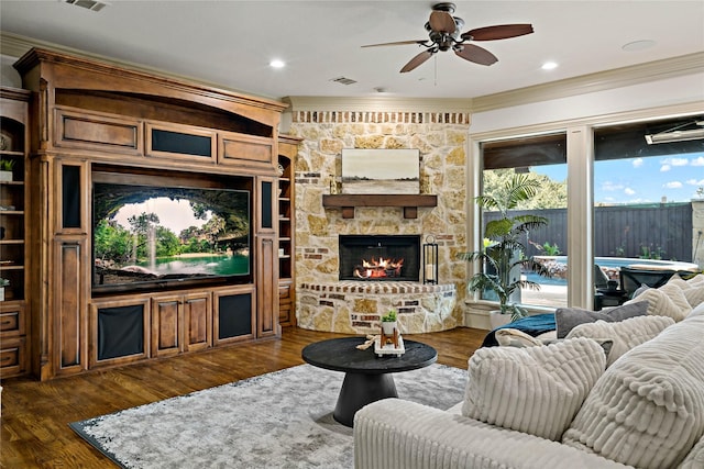 living area featuring crown molding, ceiling fan, a stone fireplace, visible vents, and dark wood-style floors