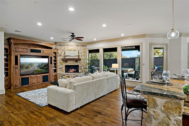 living room featuring a ceiling fan, visible vents, crown molding, a fireplace, and dark wood-style floors