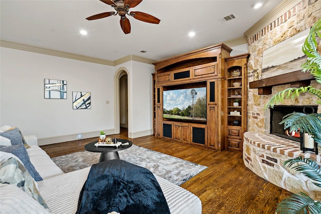 living room featuring visible vents, ornamental molding, wood finished floors, a stone fireplace, and arched walkways
