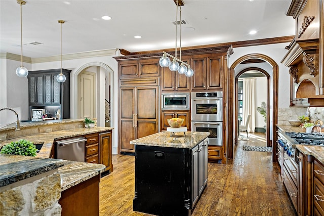 kitchen with crown molding, arched walkways, wood finished floors, a sink, and built in appliances