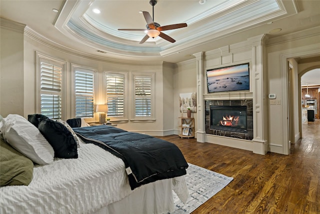bedroom with crown molding, multiple windows, a fireplace, wood finished floors, and a tray ceiling