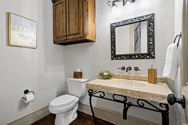 half bathroom with baseboards, a sink, wood finished floors, and toilet