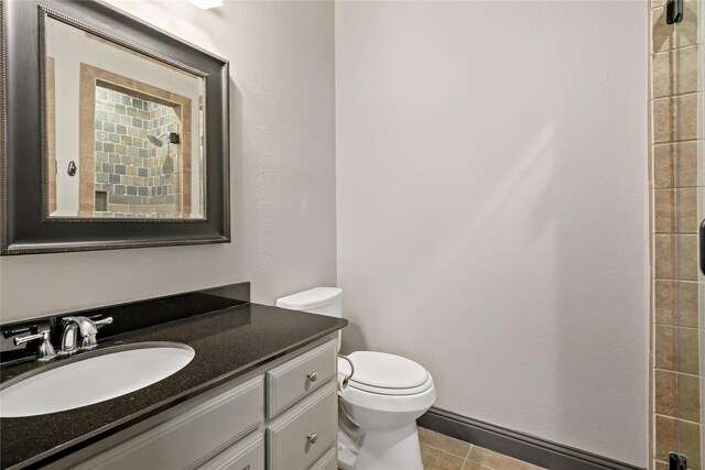 bathroom featuring vanity, a tile shower, toilet, and tile patterned floors