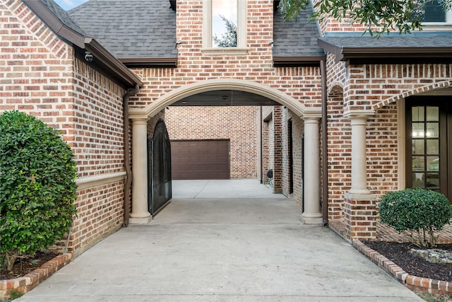 property entrance featuring brick siding, driveway, roof with shingles, and a garage