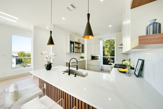 kitchen with pendant lighting, backsplash, white cabinetry, and sink