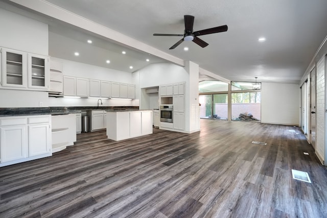 kitchen featuring stainless steel oven, ceiling fan, white cabinets, vaulted ceiling with beams, and a kitchen island