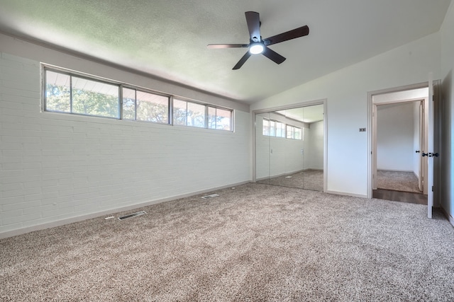 unfurnished bedroom with carpet flooring, brick wall, ceiling fan, a closet, and lofted ceiling