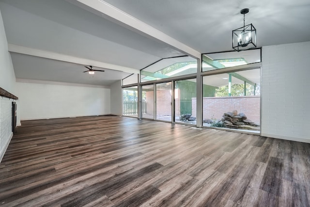 unfurnished living room with ceiling fan with notable chandelier, dark hardwood / wood-style flooring, lofted ceiling with beams, and brick wall