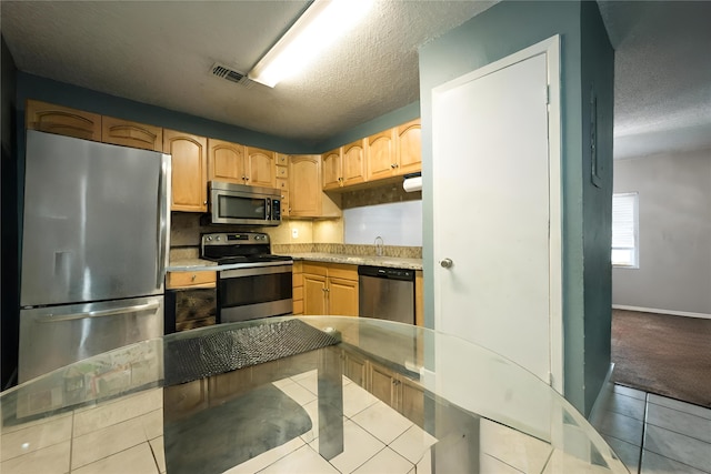 kitchen featuring light brown cabinetry, appliances with stainless steel finishes, a textured ceiling, and light tile patterned floors