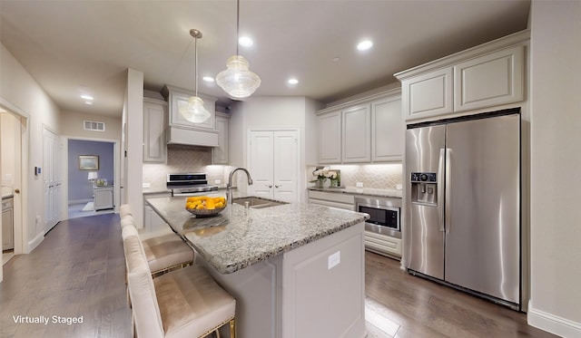 kitchen featuring a kitchen island with sink, sink, light stone counters, and stainless steel appliances