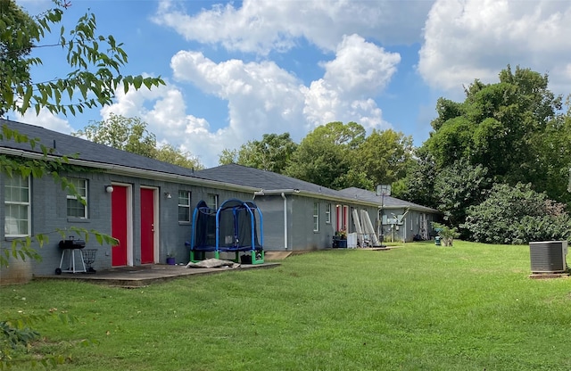 rear view of property featuring a yard, a patio area, a trampoline, and central AC unit