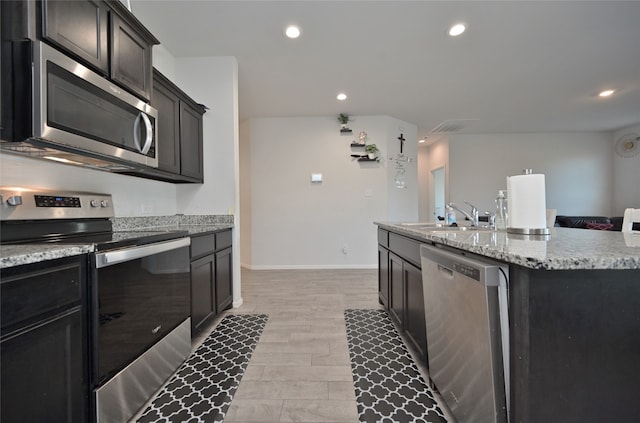 kitchen featuring light stone countertops, sink, an island with sink, light hardwood / wood-style floors, and stainless steel appliances