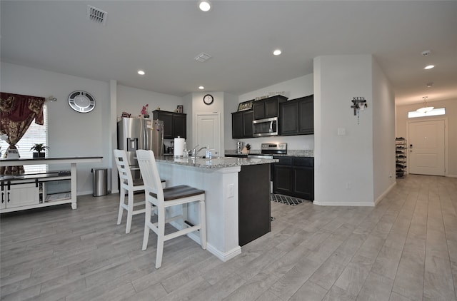 kitchen featuring appliances with stainless steel finishes, a kitchen breakfast bar, light hardwood / wood-style floors, light stone counters, and a center island with sink