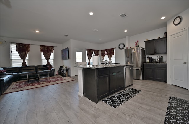 kitchen featuring appliances with stainless steel finishes, a kitchen island with sink, light stone counters, and plenty of natural light