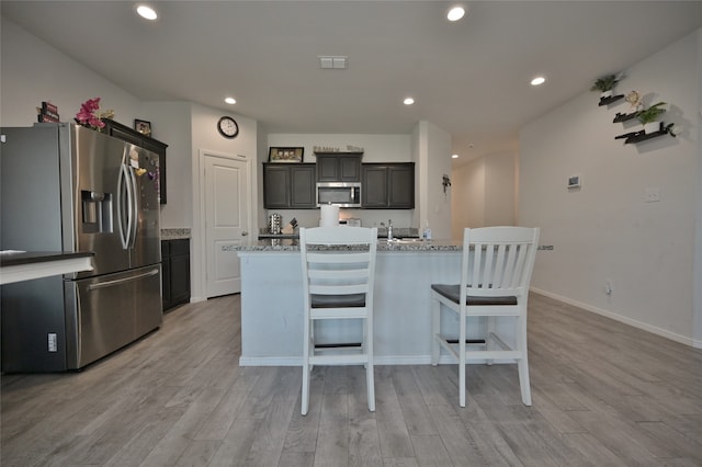 kitchen featuring stainless steel appliances, a center island with sink, and light wood-type flooring