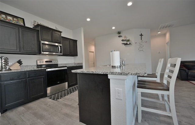 kitchen with appliances with stainless steel finishes, a breakfast bar area, a kitchen island with sink, and light hardwood / wood-style floors