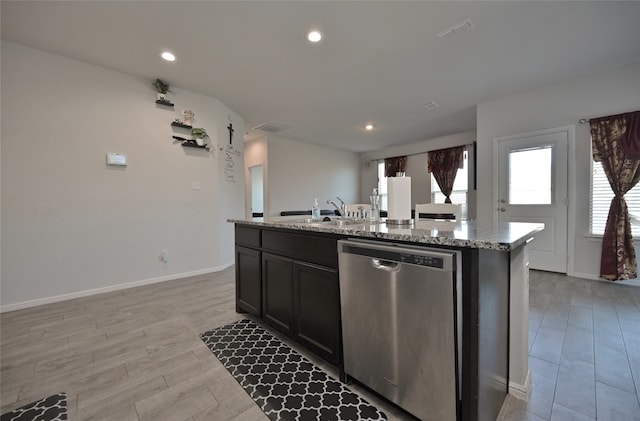 kitchen featuring sink, stainless steel dishwasher, light stone counters, light hardwood / wood-style flooring, and a center island with sink