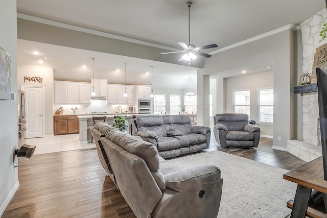 living room featuring crown molding, a stone fireplace, light wood-type flooring, and ceiling fan