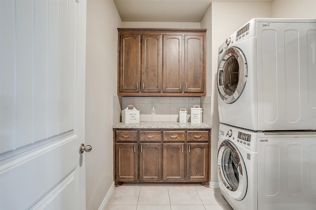 washroom featuring stacked washing maching and dryer, cabinets, and light tile patterned floors