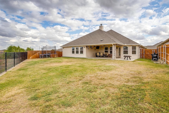 rear view of house with a yard, a trampoline, and a patio