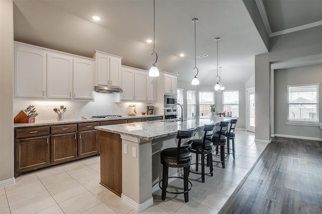 kitchen with light wood-type flooring, an island with sink, hanging light fixtures, white cabinetry, and stainless steel appliances