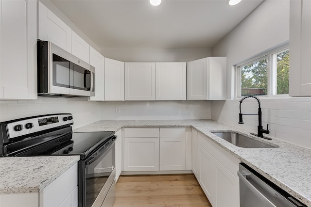 kitchen with light stone countertops, sink, stainless steel appliances, white cabinets, and light hardwood / wood-style flooring