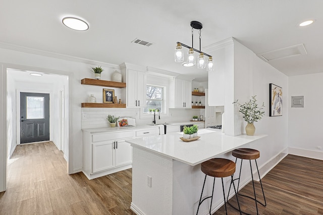 kitchen with pendant lighting, a breakfast bar, white cabinets, hardwood / wood-style flooring, and kitchen peninsula