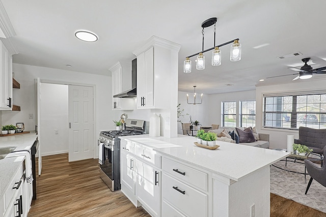 kitchen with white cabinetry, gas stove, hanging light fixtures, and wall chimney exhaust hood