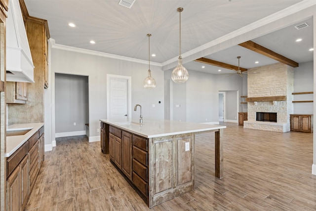 kitchen featuring a large island, sink, hanging light fixtures, a stone fireplace, and light hardwood / wood-style floors