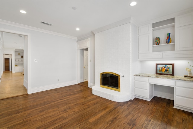 unfurnished living room featuring ornamental molding, built in desk, a fireplace, and dark hardwood / wood-style flooring