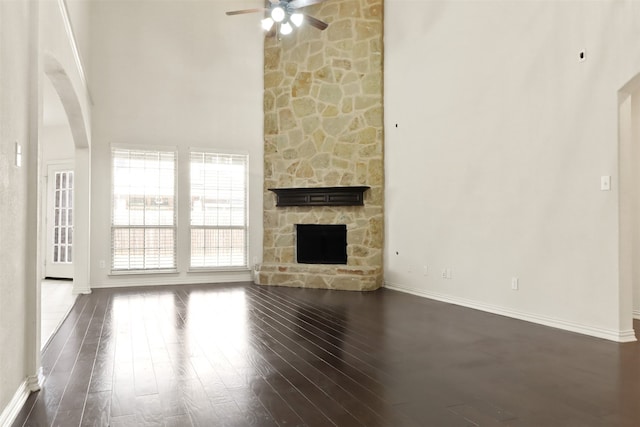 unfurnished living room with ceiling fan, a high ceiling, a fireplace, and dark hardwood / wood-style flooring