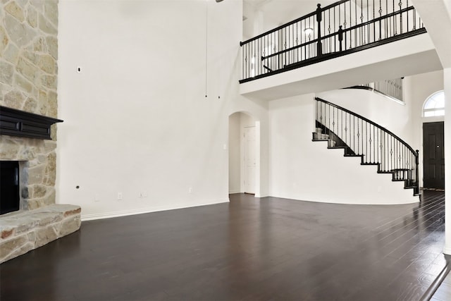 unfurnished living room with a high ceiling, a stone fireplace, and dark hardwood / wood-style flooring