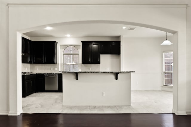 kitchen featuring dark stone countertops, light wood-type flooring, a wealth of natural light, and stainless steel dishwasher