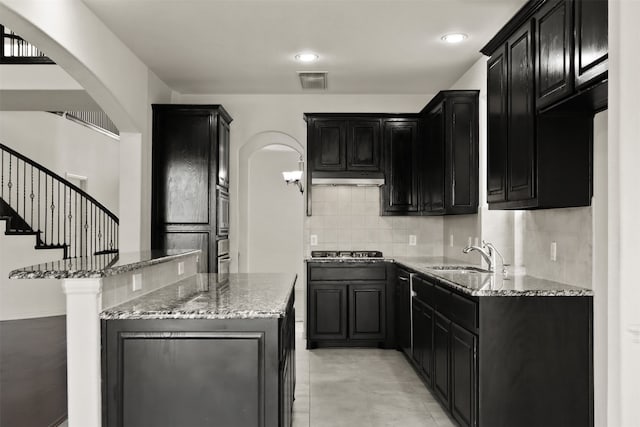 kitchen featuring stone counters, sink, a center island, stainless steel gas stovetop, and decorative backsplash