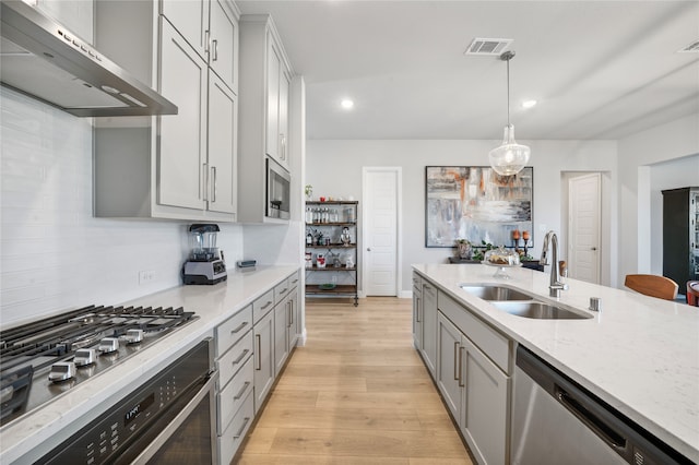 kitchen with hanging light fixtures, light wood-type flooring, stainless steel appliances, wall chimney exhaust hood, and sink